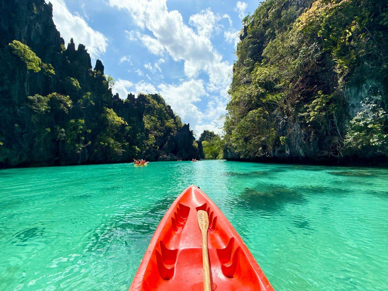 A red kayak in a turquoise lagoon between limestone cliffs.